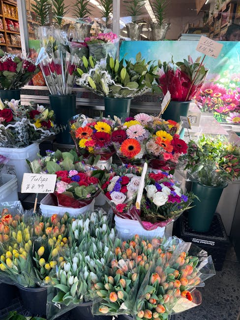 A vibrant display of fresh floral arrangements at a flower stall, featuring bouquets of tulips in shades of yellow, orange, and white, alongside smaller mixed flower bouquets including pink, purple, o